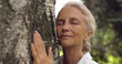 Portrait of senior gray haired woman hugging tree.