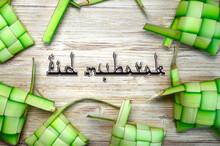 Eid Mubarak Text With Ketupat Casing On Wooden Table