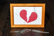 Shards of glass from a photo frame on a dark wooden table. The paper heart is torn in two.
