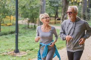 Wall Mural - Smiling senior couple jogging in the park. Sports activities for elderly people.