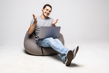 Portrait of attractive cheerful guy sitting in chair using laptop calling contact isolated over white background