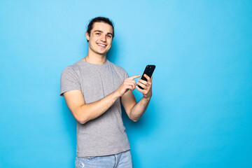 Serious male blogger uses modern smartphone, has attentive gaze at display isolated over blue background. People and modern technology concept