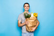 © F8  \ Suport Ukraine - Young man holding two paper bags with food from the grocery store on blue background