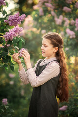 Wall Mural - Portrait of cute schoolgirl in school uniform looking at branches of lilac in spring