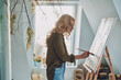 © gstockstudio - Side view of attractive young woman painting in art studio