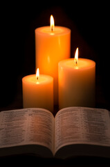 Wall Mural - Three Pillar Candles Burning in a Dark Room with a Bible