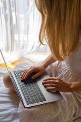 Girl works with a laptop and a smartphone in bed at home or in hotels. Distant work. Office at home. Woman in the bedroom is typing on a laptop, distance learning for students, surfing the Internet