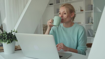 Wall Mural - Beautiful young woman drinking coffee while using laptop at home 