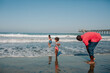 © Erin Brant/Stocksy - Girls wade in waves while dad rolls up jeans