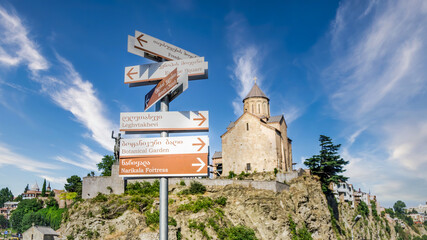 Wall Mural - Tbilisi, Georgia - August 2015: Directional road signs in Tblisi with Metekhi Church in the background