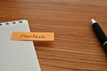 Poster - There is sticky note with the word of Martech which is an abbreviation for Marketing and Technology on the desk with a pen.