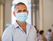 Portrait of man in blue shirt and face mask standing indoors