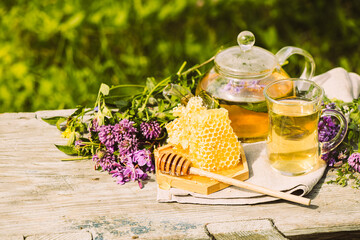 Wall Mural - Tea with fresh leaves of summer herbs clover natural liquid honeycomb in glass teapot cup on a rustic wooden background