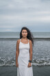 © Aleksandr - Portrait of charming young mongol woman in bright grey dress standing on the beach. Black long curly hair. Looking at camera with copy space. Romantic photo.
