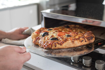 Wall Mural - Closeup shot of a male cook hand removing baked pizza from the oven