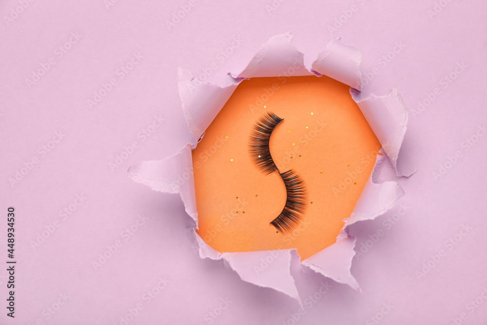 Composition with false eyelashes visible through torn paper