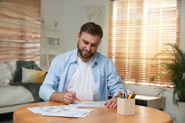 Young man coloring antistress picture at table indoors