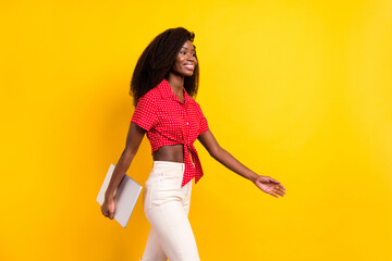 Poster - Photo of young happy smiling afro girl go walk look copyspace hold laptop in hand isolated on yellow color background