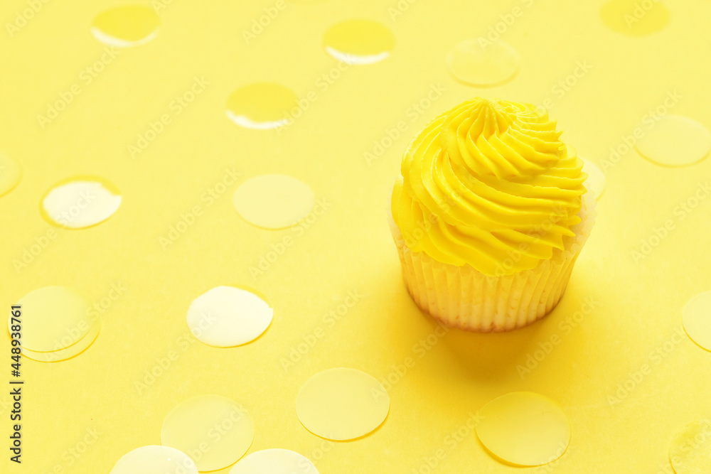 Tasty Birthday cupcake and confetti on color background