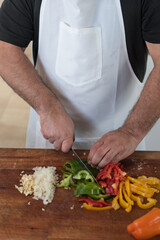 Wall Mural - Closeup shot of a male cook chopping vegetables on a wooden boar