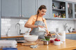 © Syda Productions - culinary, baking and people concept - happy smiling young woman cooking food on kitchen at home adding sugar to bowl