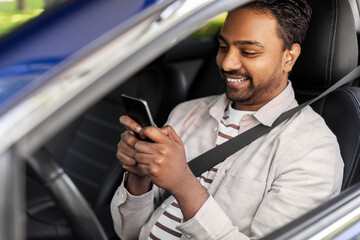 transport, people and technology concept - smiling indian man or driver using smartphone in car