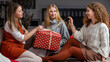 © ako-photography - three young girls sitting on the couch and having fun unwrapping Christmas presents at home