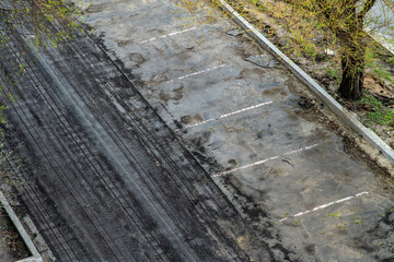 Wall Mural - Top view of a dirty parking lot with numerous tire tracks. Parking lot with partially removed asphalt surface and remnants of road markings