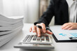 © sirichai - Close up of Businesswoman or auditor using calculator calculate business reports and paperwork chart on desk in workplace, Accountant making financial statements, financing and accounting concept.