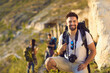 © Studio Romantic - Portrait of young man with backpack and camera in mountains, copy space. Happy tourist and blurred hikers on walking tour outdoors