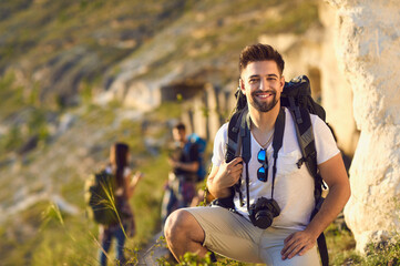Wall Mural - portrait of young man with backpack and camera in mountains, copy space. happy tourist and blurred h