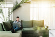 © Lena Ivanova - Young guy sitting at green sofa with gray laptop and black phone