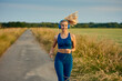 Fit vivacious young woman jogging along a footpath in open fields approaching the camera with a happy smile and ponytail flying out behind in a healthy active lifestyle concept