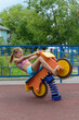 Teen girl sits on toy wooden motorbike on playground