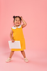 Canvas Print - full length of happy asian toddler kid in yellow dress holding digital tablet on pink