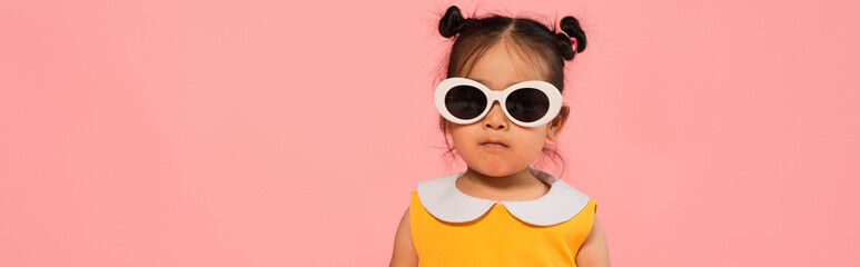 Canvas Print - asian toddler girl in dress and sunglasses posing isolated on pink, banner