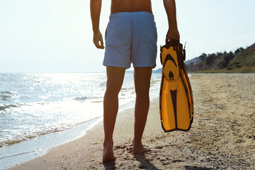 Back view of man with flippers walking on beach, closeup