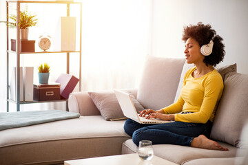 Wall Mural - African woman working from home at the computer during self-isolation and quarantine. Coronavirus outbreak and flu covid epidemic. Copy space. Smiling young african american teen girl wear headphones 