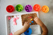 Baby Toddler plays with cereals, sorts toy figures by color. Child plays with tweezers, Montessori activities, fine motor development and sensory play, top view