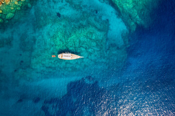 Wall Mural - aerial top down view of a sailing boat anchored on a emerald reef in the turquoise sea