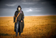 A Man In A Gas Mask Walks Through A Scorched Field. He Holds A Radiometer In His Hand.