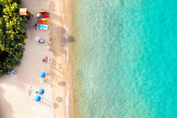 Wall Mural - View from above, stunning aerial view of a white sand beach bathed by a turquoise water and relaxed people under some beach umbrellas at sunset. Cala di volpe beach, Costa Smeralda, Sardinia, Italy.
