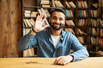 Wall Mural - Video meeting with a happy indian man, cheerful guy waving and looking at the camera on a screen. Middle-aged mixed-race eastern male employee takes a part in virtual conference, video call