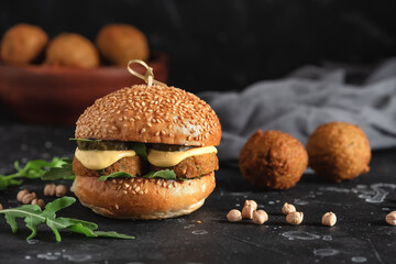 Vegan falafel burger with sauce, pickled cucumber and arugula on a black stone background. Selective focus.