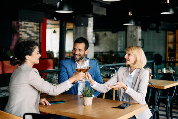 Group of happy business colleagues toasting with wine while celebrating cafe.