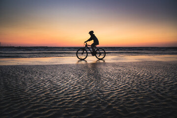 Silhouette of a boy on a bicycle riding on a small portion of sand in the middle of the water from the baltic sea. Dramatic stunning sunset colors. Estonia, Europe