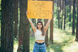 young beautiful woman volunteer activist in the forest with a poster save the forest
