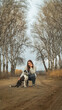 © MARALEM - Mujer arrodillada junto a su perro en medio de un camino de tierra, mujer acariciando a su perro en medio de los árboles , perro blanco con manchas negras