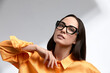 © Georgii - Girl in bright clothes and sunglasses, brunette, stylishly dressed, on a gray background on a gray background, advertising glasses, copies of space, close-up