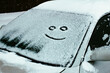 a sad and cheerful face painted in the first snow on the windshield of a car, in the form of a smiley. foreground and background blurred with bokeh effect